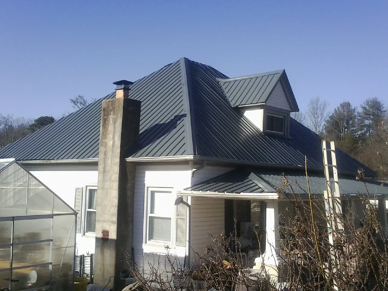 Dark blue standing seam metal roof on a white farmhouse with dormer — Slate & Tile Roof Repair by Roofing Brothers in Mishicot