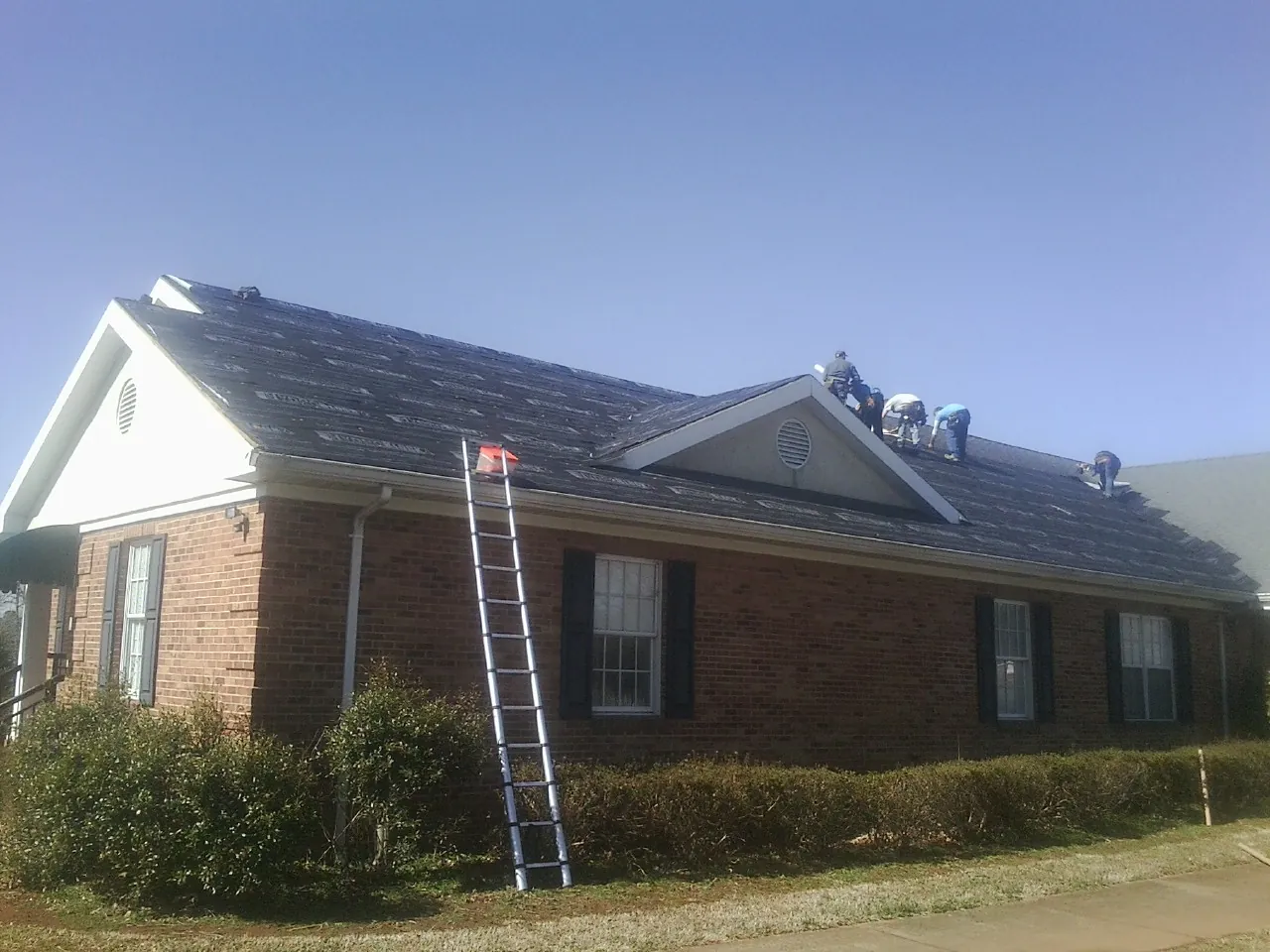 Crew tearing shingles off a brick ranch roof with a ladder set — Emergency Roof Repair work by our crew in Mishicot