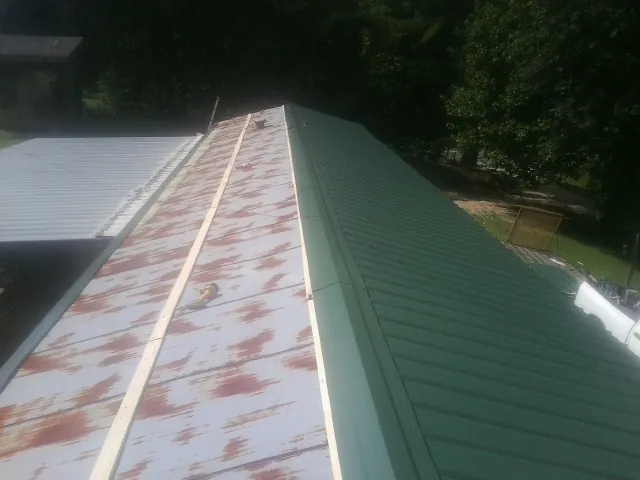 Old rusted panels beside newly installed green metal roofing — Wind Damage Roof Repair by Roofing Brothers in Mishicot