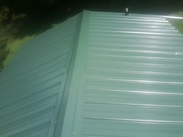 New green metal panels meeting at the ridge of a roof — Flat Roof Repair work by our crew in Mishicot