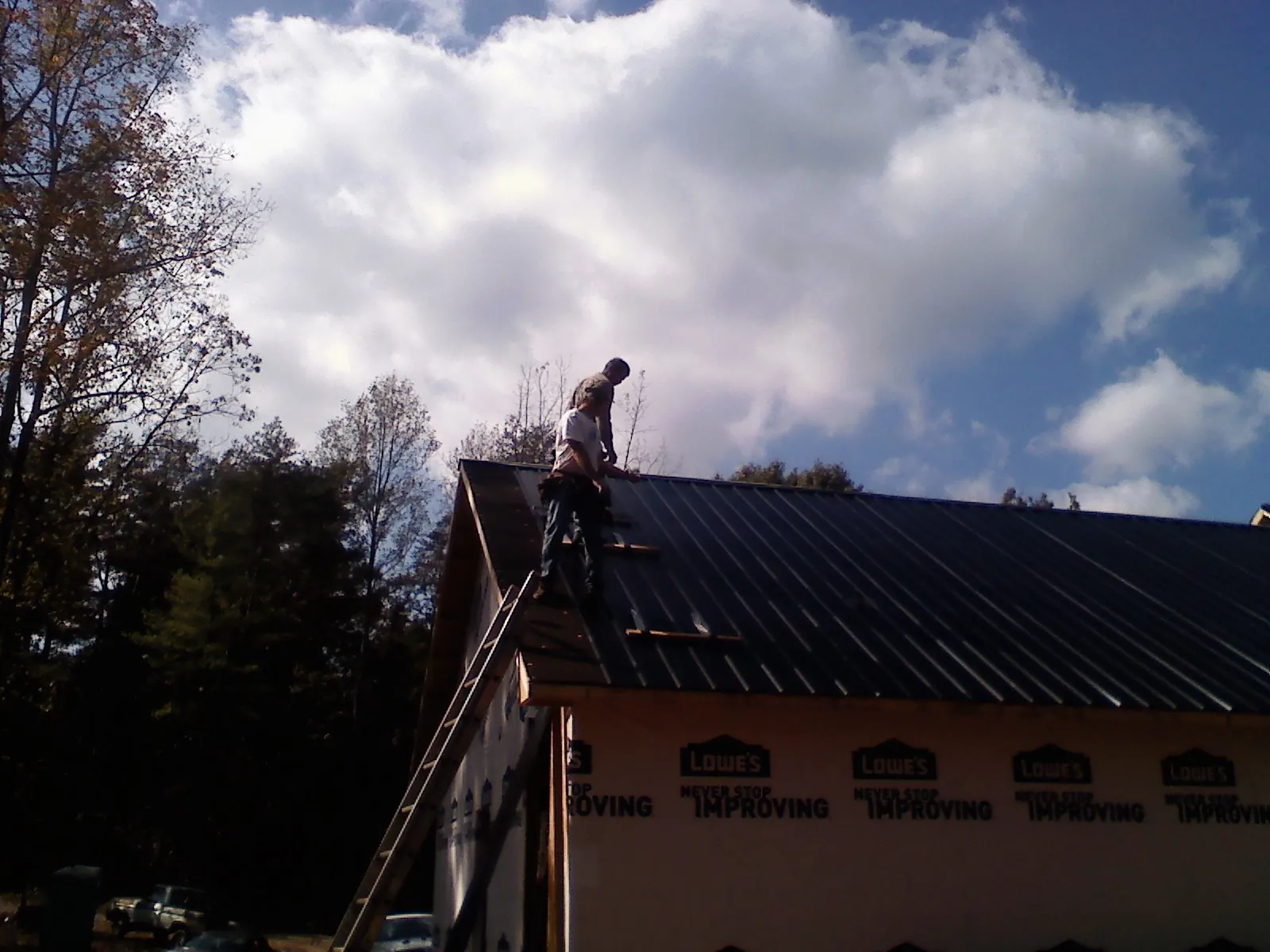 Roofer fastening dark metal panels high against a cloudy sky, from a Roof Inspection job in Mishicot